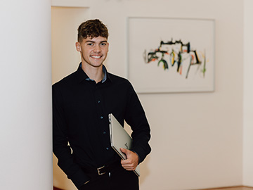 Mitarbeiter lacht und hat Laptop unter dem Arm