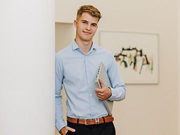 Mitarbeiter sitzt am Schreibtisch, schreibt und lacht