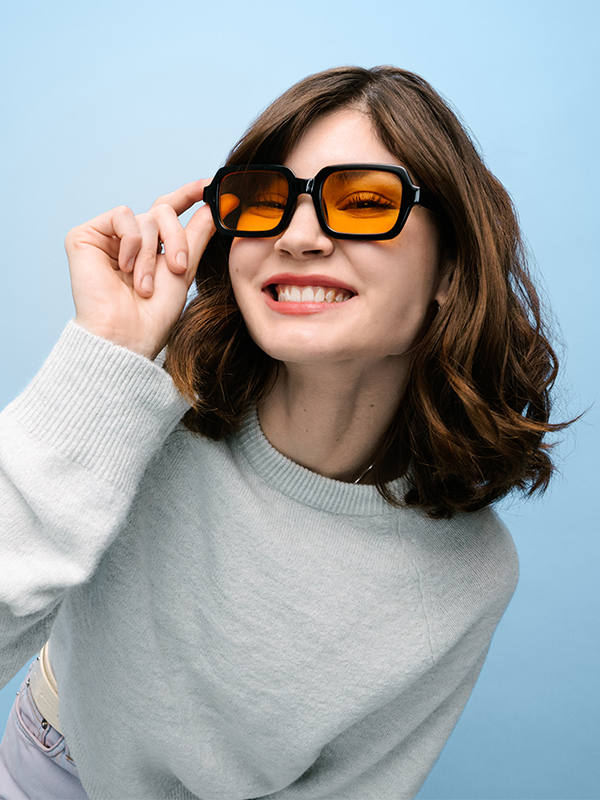 Junge Dame mit gelber Sonnenbrille vor blauem Hintergrund