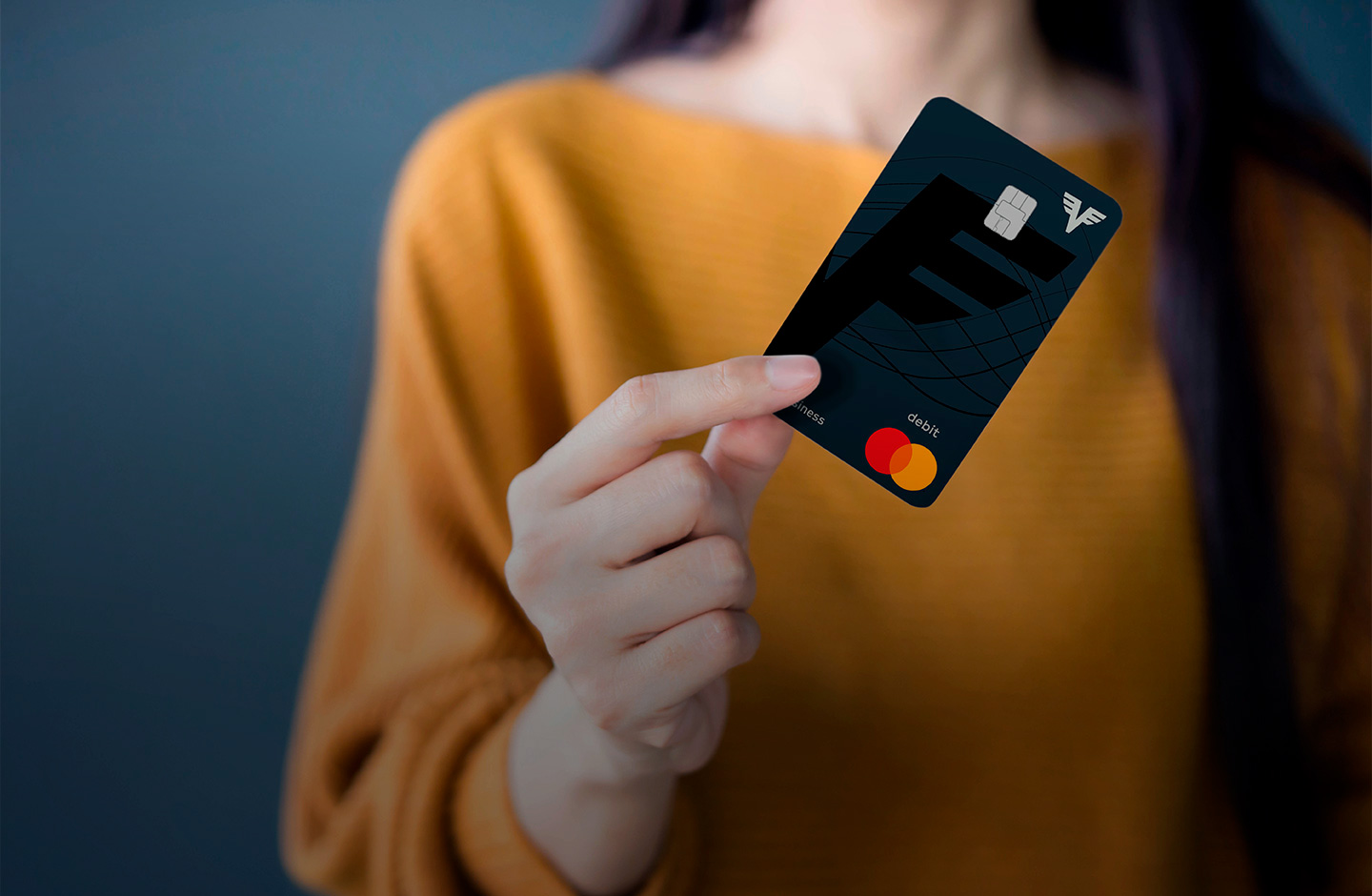 Eine Frau in einem gelben Pullover hält die Volksbank Debit Mastercard Business in der Hand. Man kann ihr Gesicht nicht sehen.